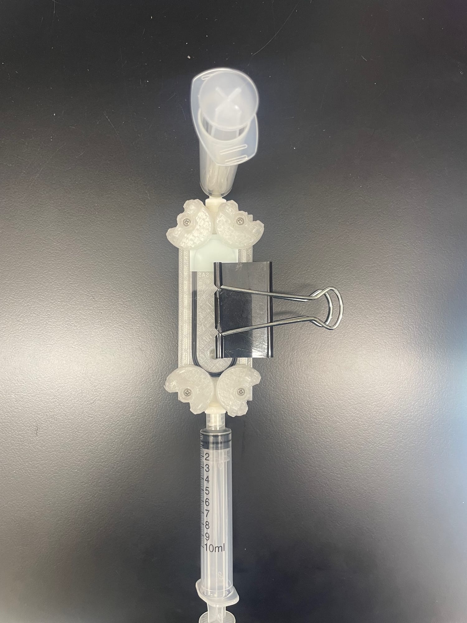 A clear 3D-printed filter device with a binder clip and Luer fittings, held vertically