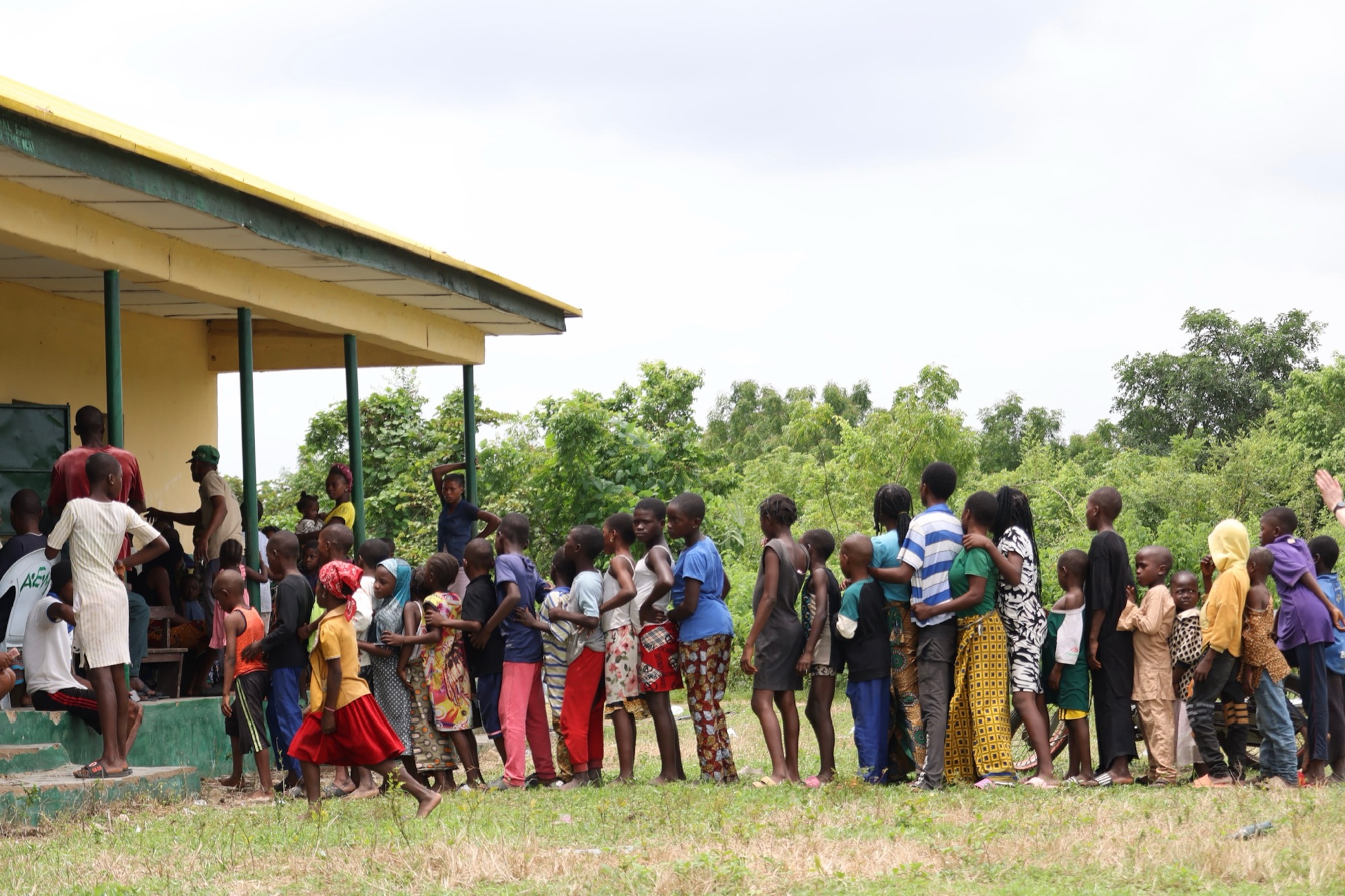 A long line of children and families waits outside a schoolhouse for a community screening