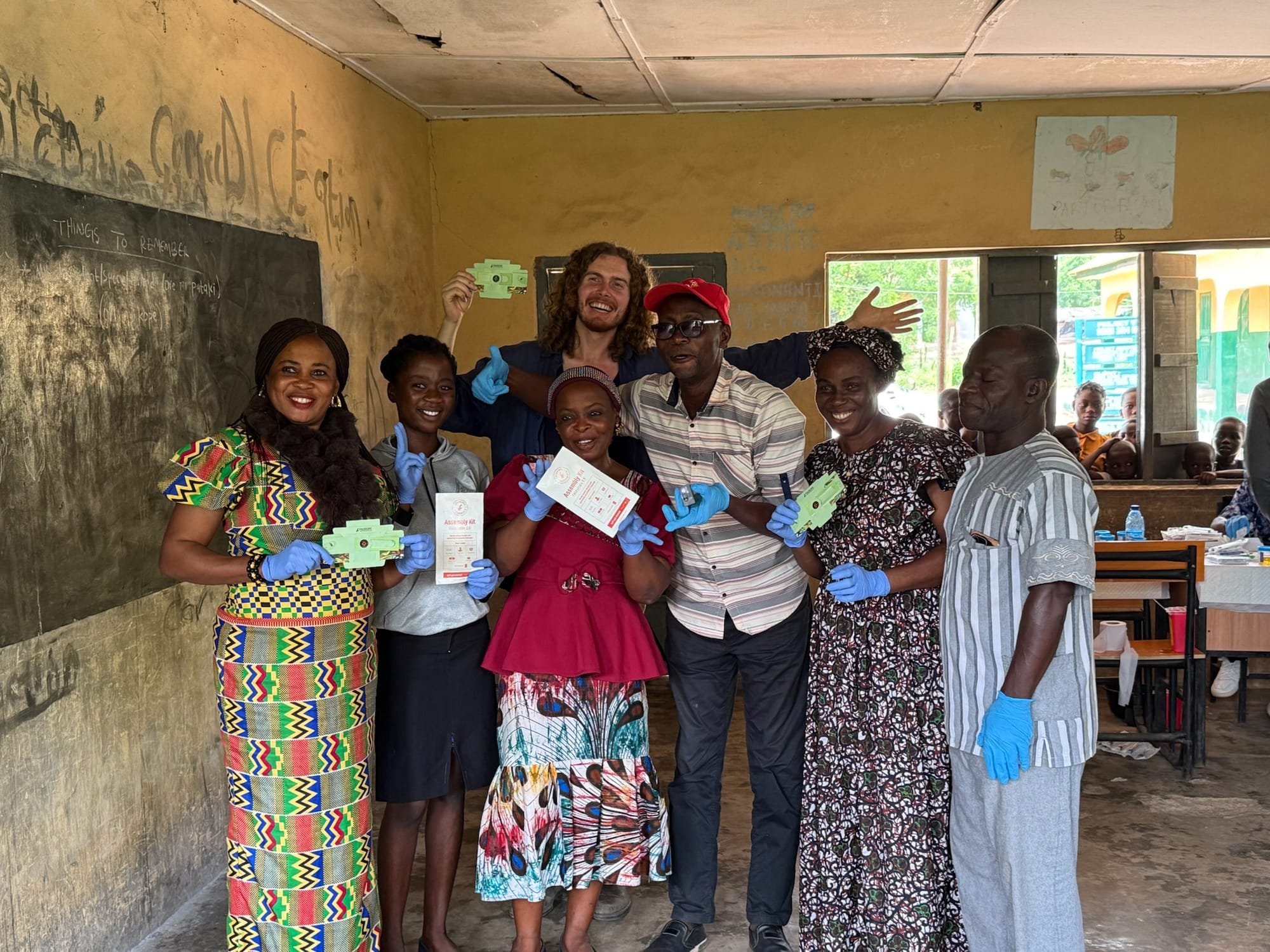 The community health extension worker team and HIYH researchers pose in a classroom holding Foldscopes and SchistoFilter cards