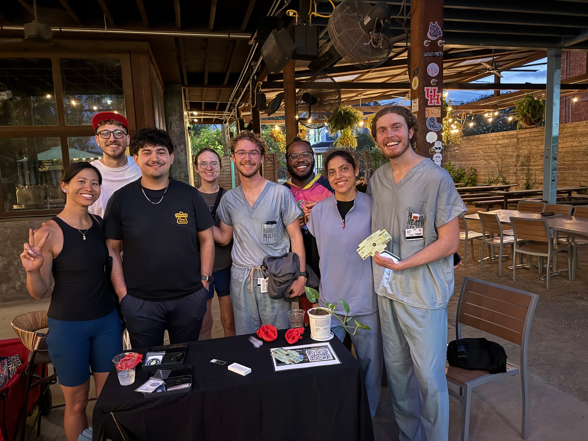 The Houston team poses behind a table of Foldscope demos under string lights at an outdoor venue