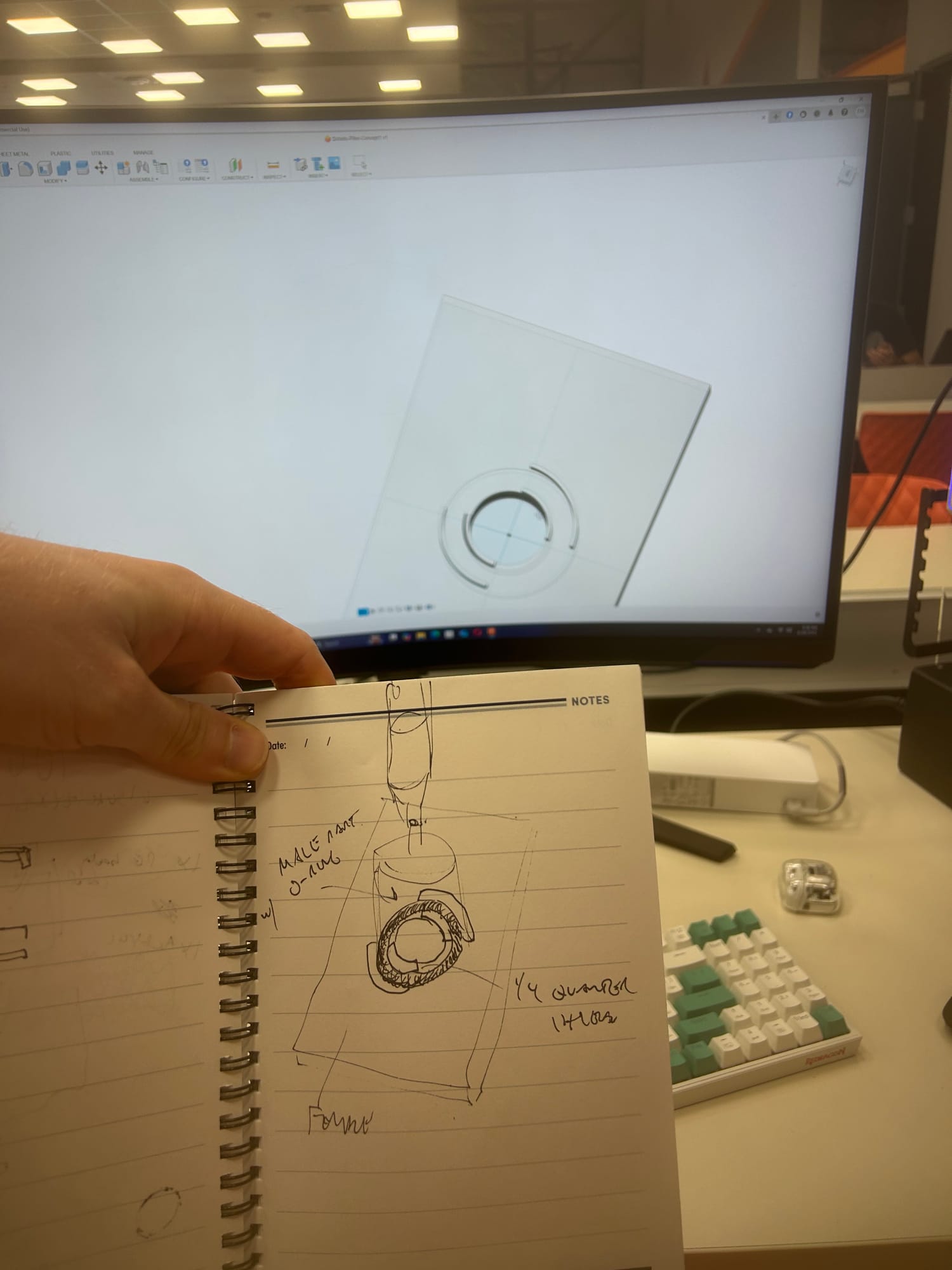A notebook sketch of a threaded fitting held up in front of a CAD model on a monitor