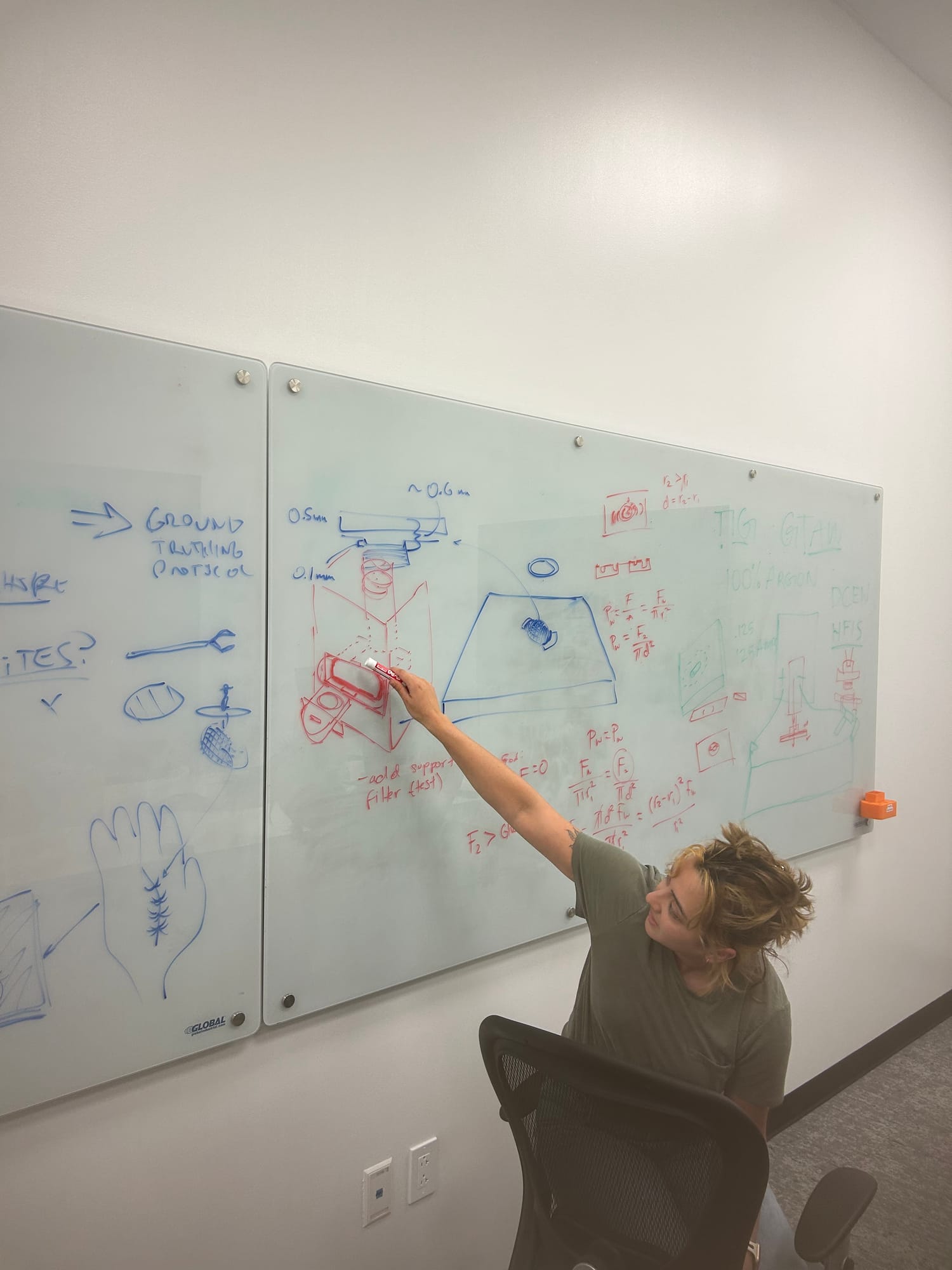 A team member sketches a device on a large whiteboard covered in diagrams