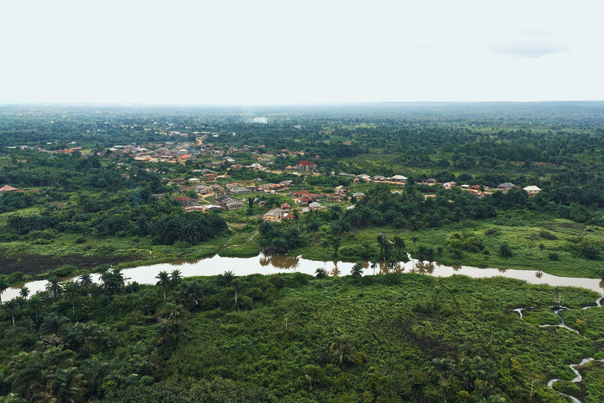 Aerial view of a riverside town, a winding river, and surrounding forest under an overcast sky
