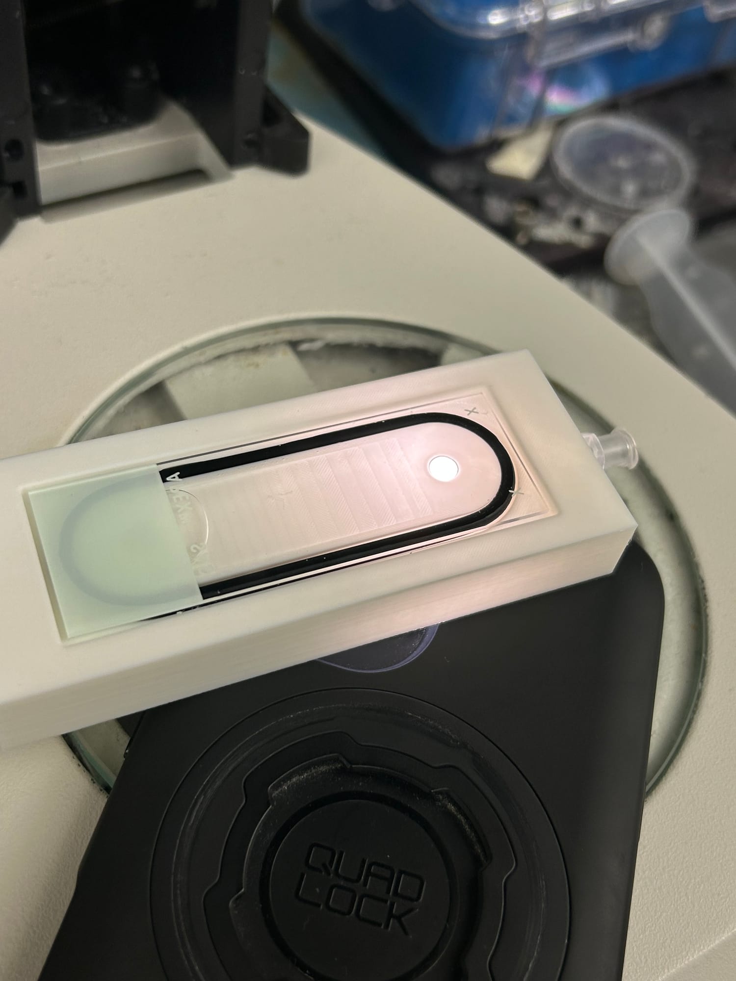 A phone flashlight shining up through a device on a microscope stage