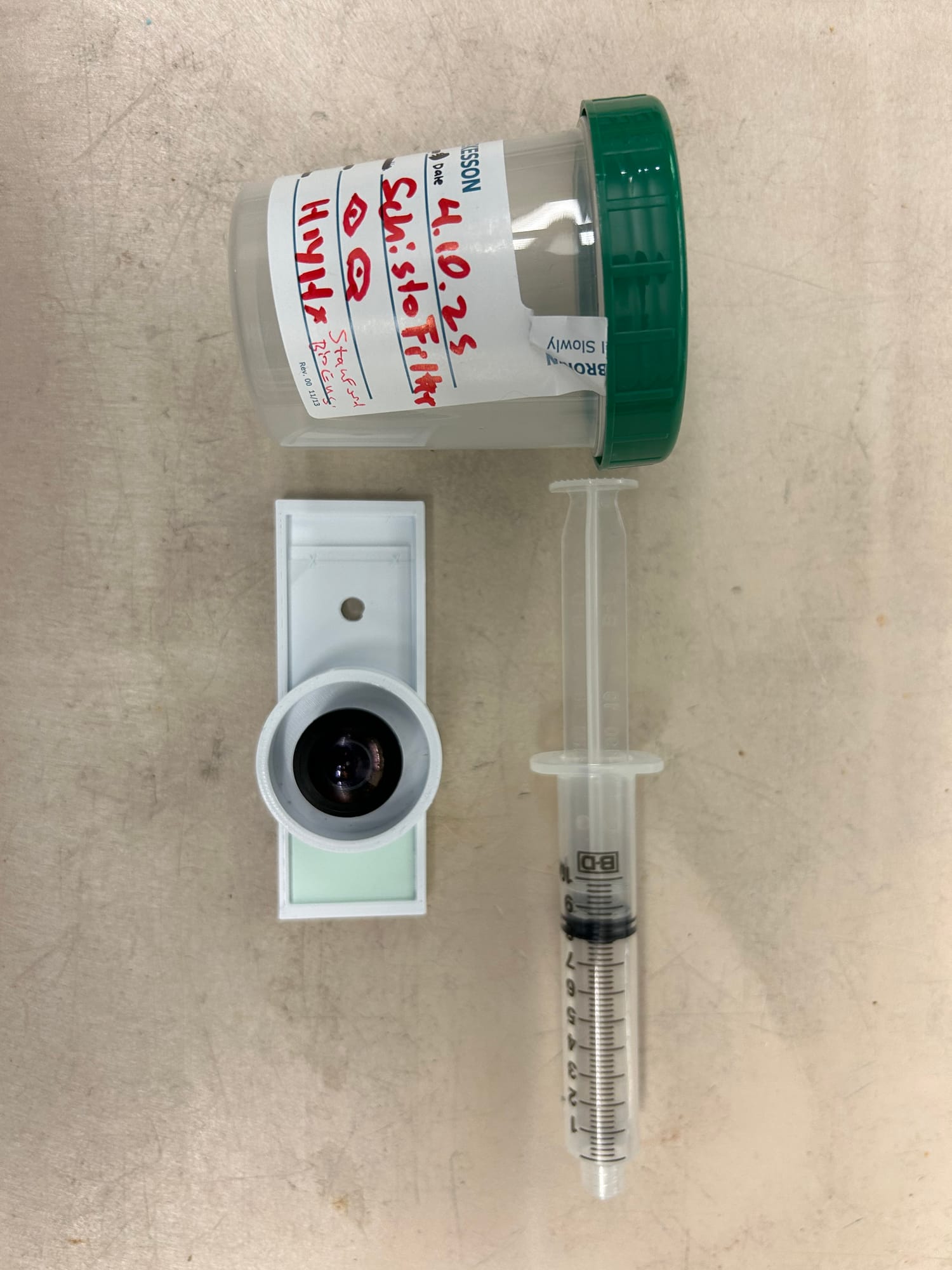 A white 3D-printed wedge device holding a single glass slide, with a fish-eye lens and syringe